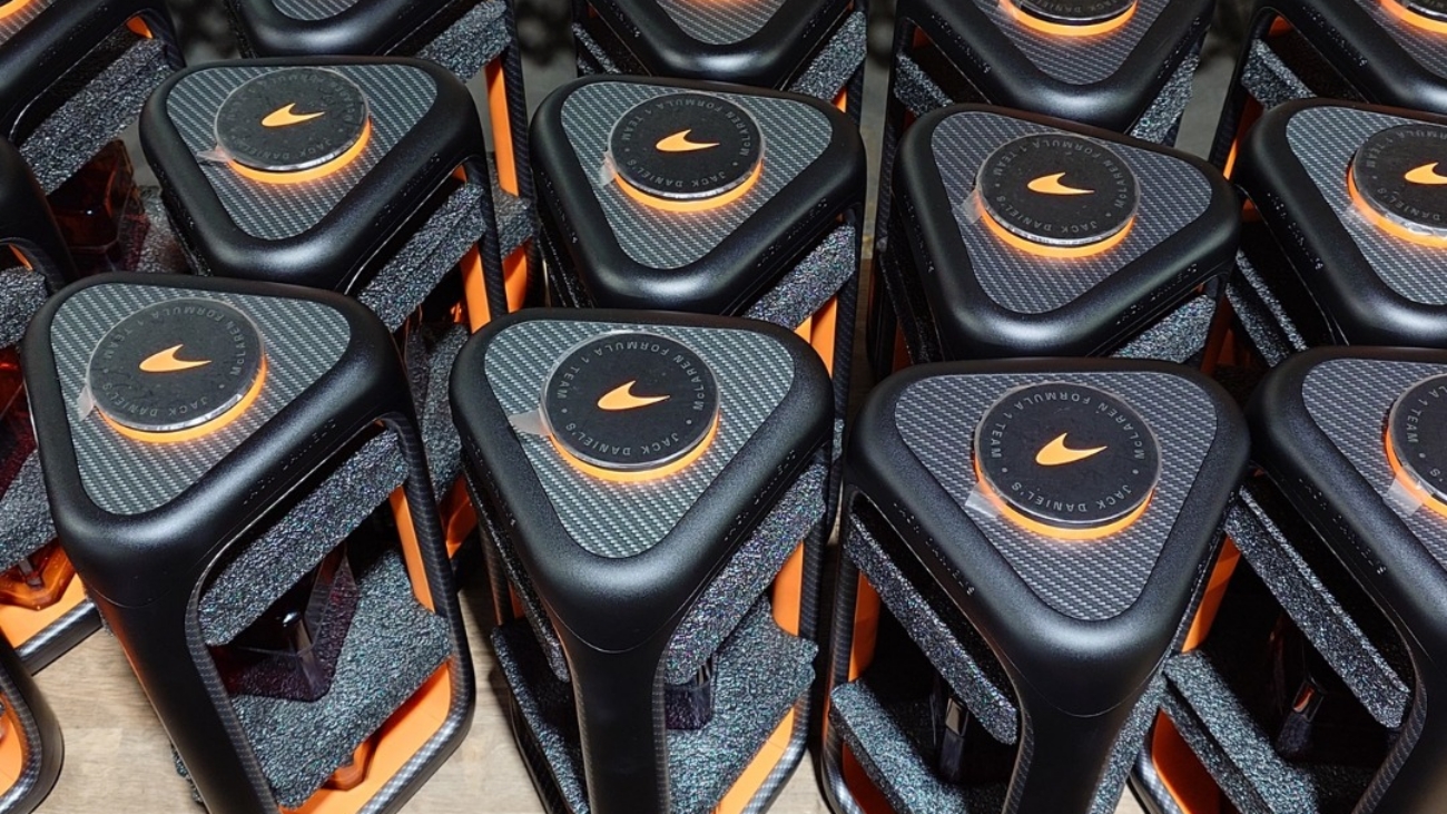 Row of black and orange sports bottles on a factory line, with orange caps and textured tops, rows ready for packaging in the background.