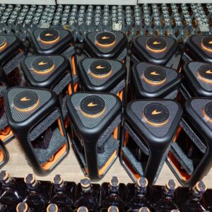 Row of black and orange sports bottles on a factory line, with orange caps and textured tops, rows ready for packaging in the background.