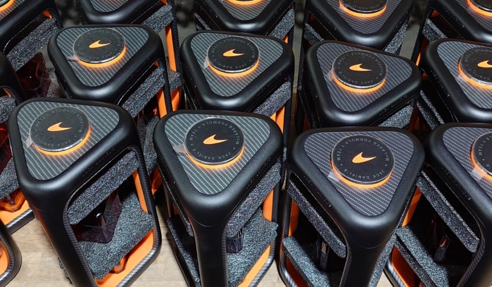 Row of black and orange sports bottles on a factory line, with orange caps and textured tops, rows ready for packaging in the background.