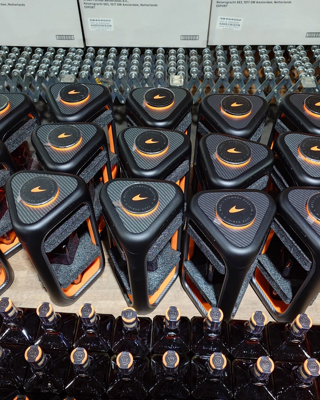 Row of black and orange sports bottles on a factory line, with orange caps and textured tops, rows ready for packaging in the background.